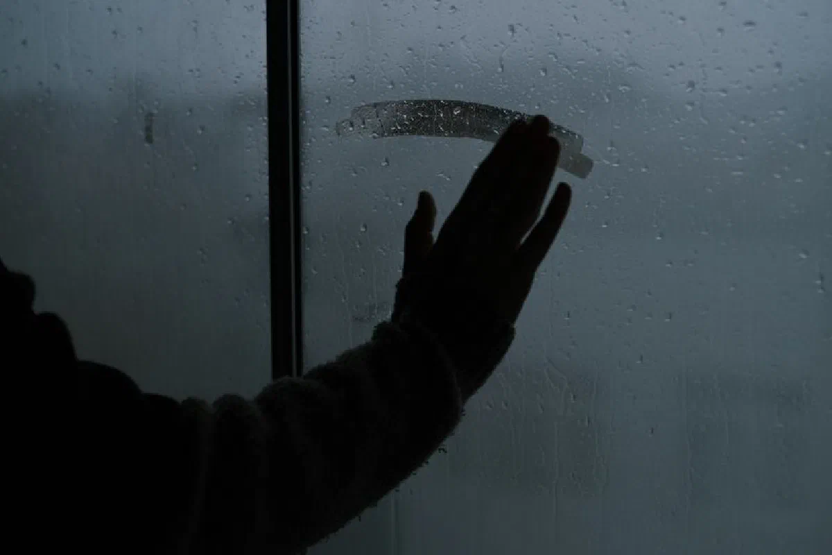 A hand touching a rainy, steamy window creating a melancholic indoor atmosphere.