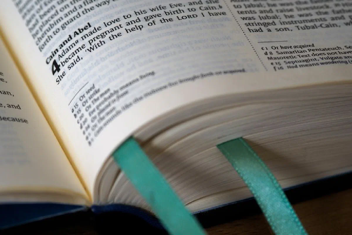 Open Bible showing Genesis, Cain and Abel story, with teal bookmarks.