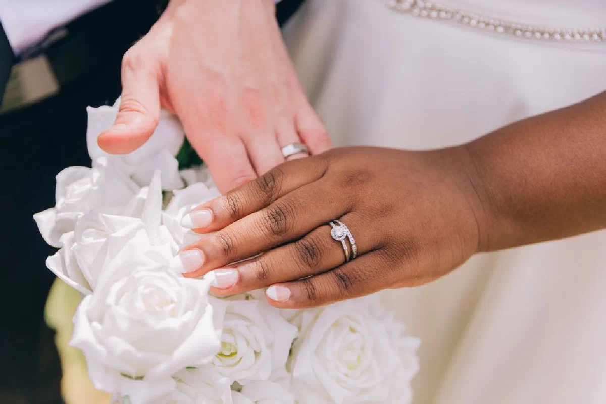 Close-up of wedding rings on a couple's hands over a white rose bouquet, symbolizing love and unity.