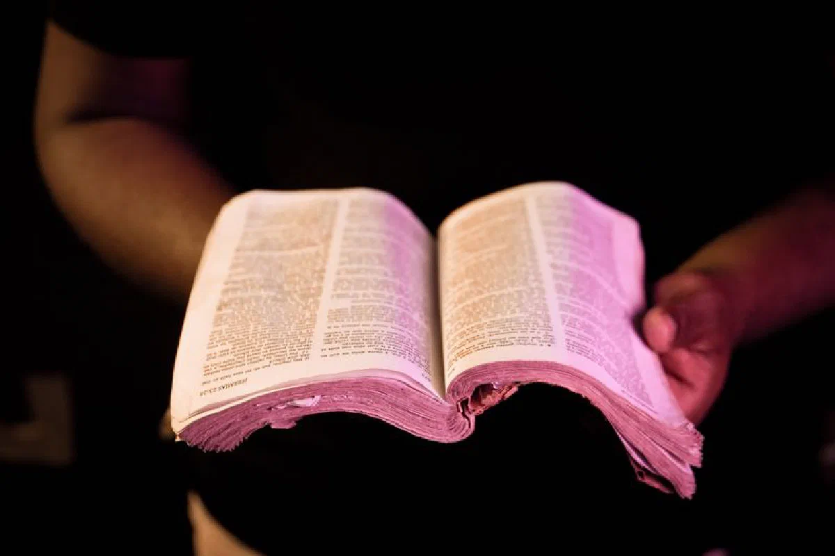 An open Bible held by a person in dim light, emphasizing spirituality and reflection.