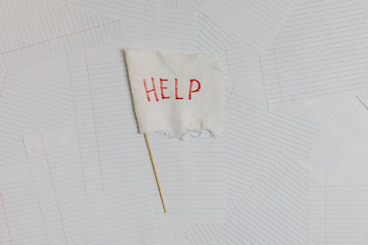 A fabric flag with 'HELP' on a scattered notepaper background, symbolizing distress or overwhelm.