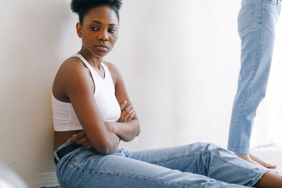 A woman sitting on the floor with crossed arms, expressing deep thought or disagreement.