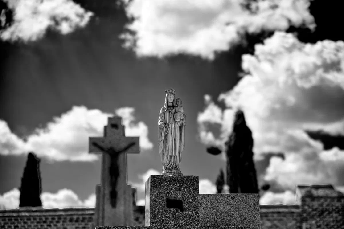 Black and white photo of Virgin Mary statue outdoors under a cloudy sky.