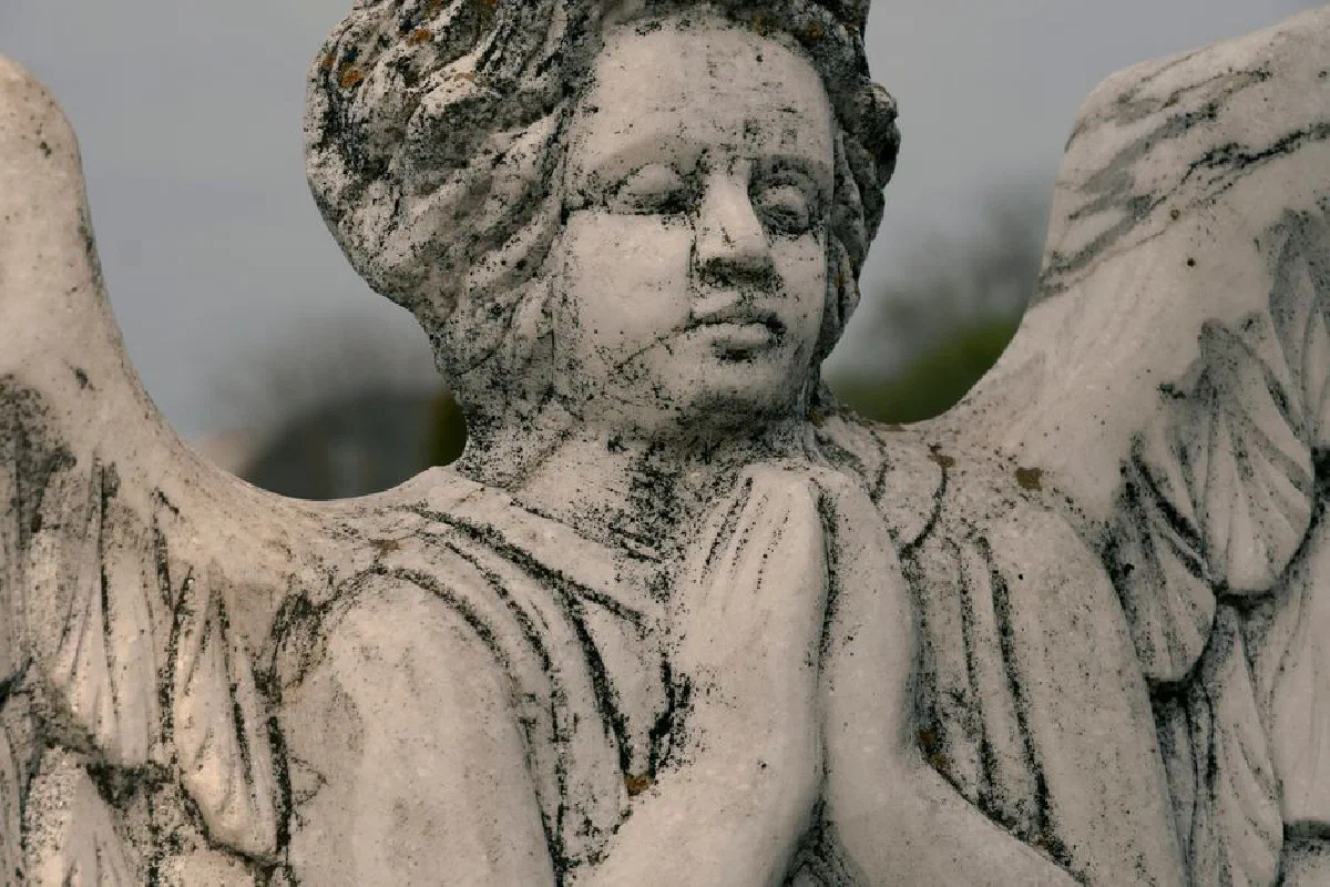 Close-up of a weathered angel statue with wings and praying hands, representing spirituality and peace.