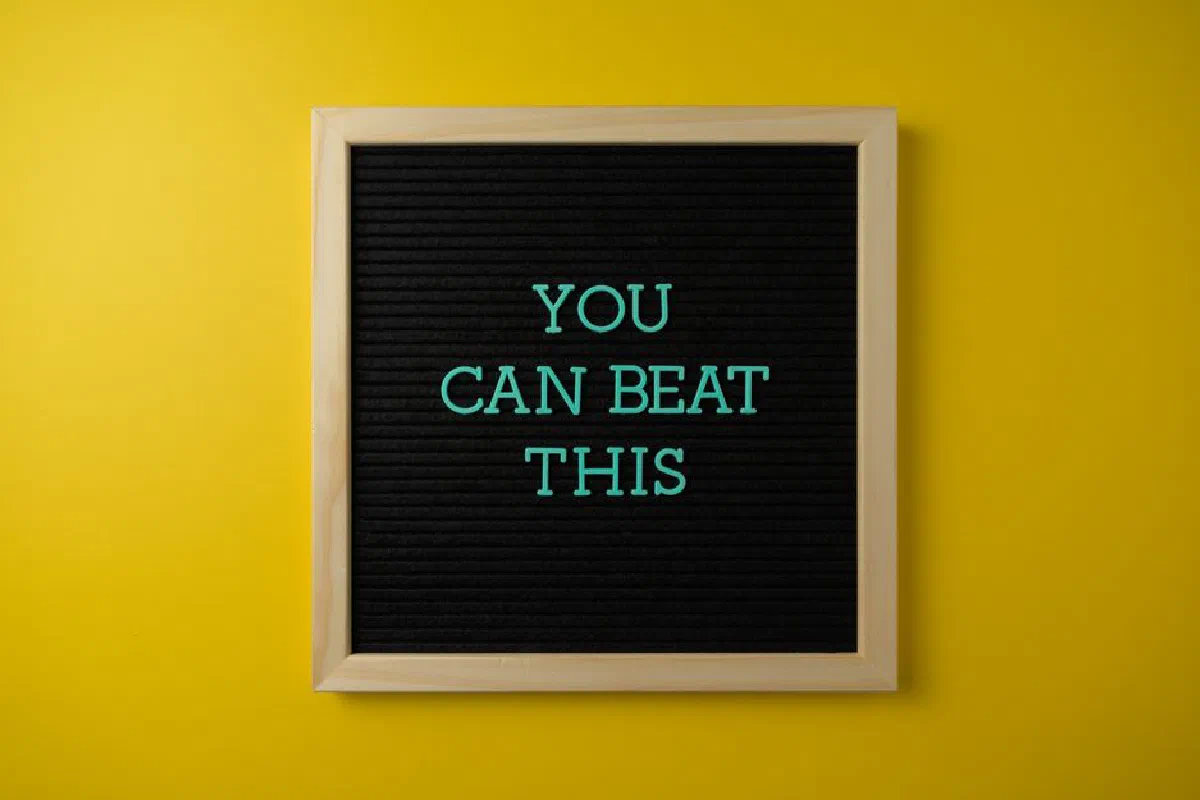 Black letter board with motivational phrase 'You Can Beat This' on vibrant yellow background.