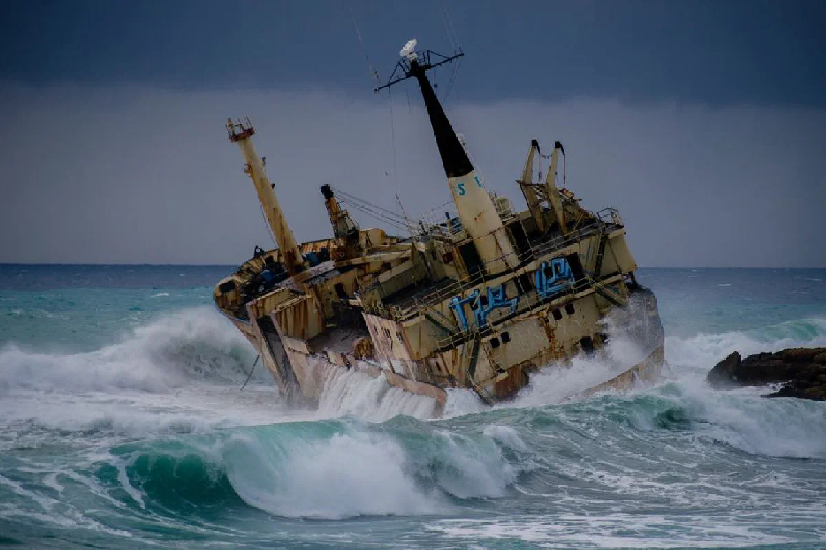 A dramatic view of the Edro III shipwreck amidst crashing waves on the Cyprus coast under dark clouds.