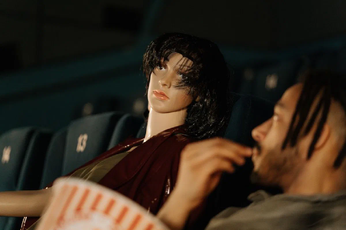 A man and a mannequin watching a movie in a theater, creating a conceptual scene.