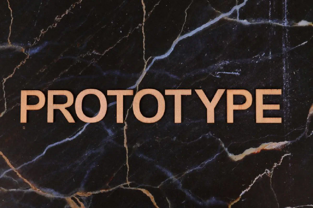 The word 'PROTOTYPE' in wooden letters on a dark marble background.