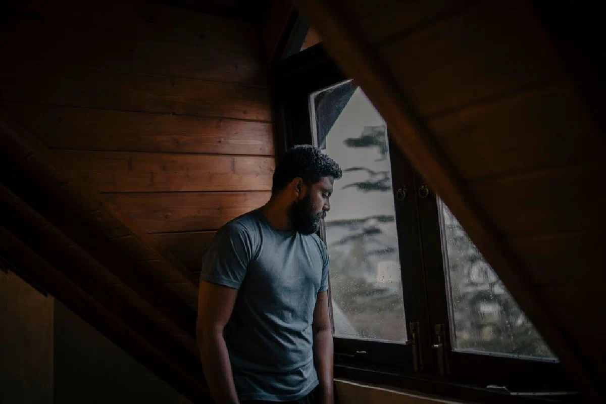 A thoughtful man stands by a window, lost in contemplation, indoors in Sri Lanka.