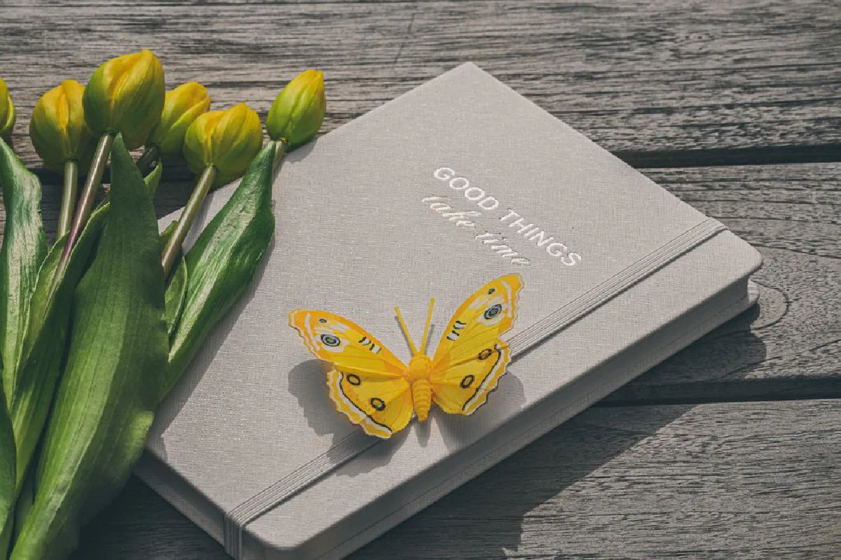 A yellow butterfly rests on a notebook with tulips, capturing a serene and inspirational moment.