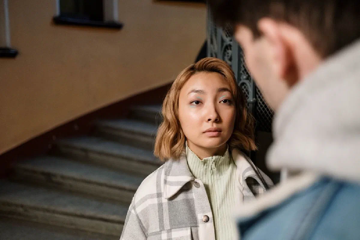 A woman stands on stairs, looking thoughtfully ahead while indoors.