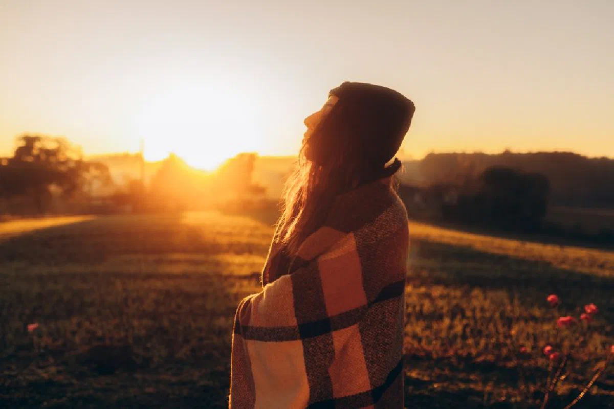 Peaceful scene of a woman wrapped in a blanket at sunrise, embracing nature's serenity.
