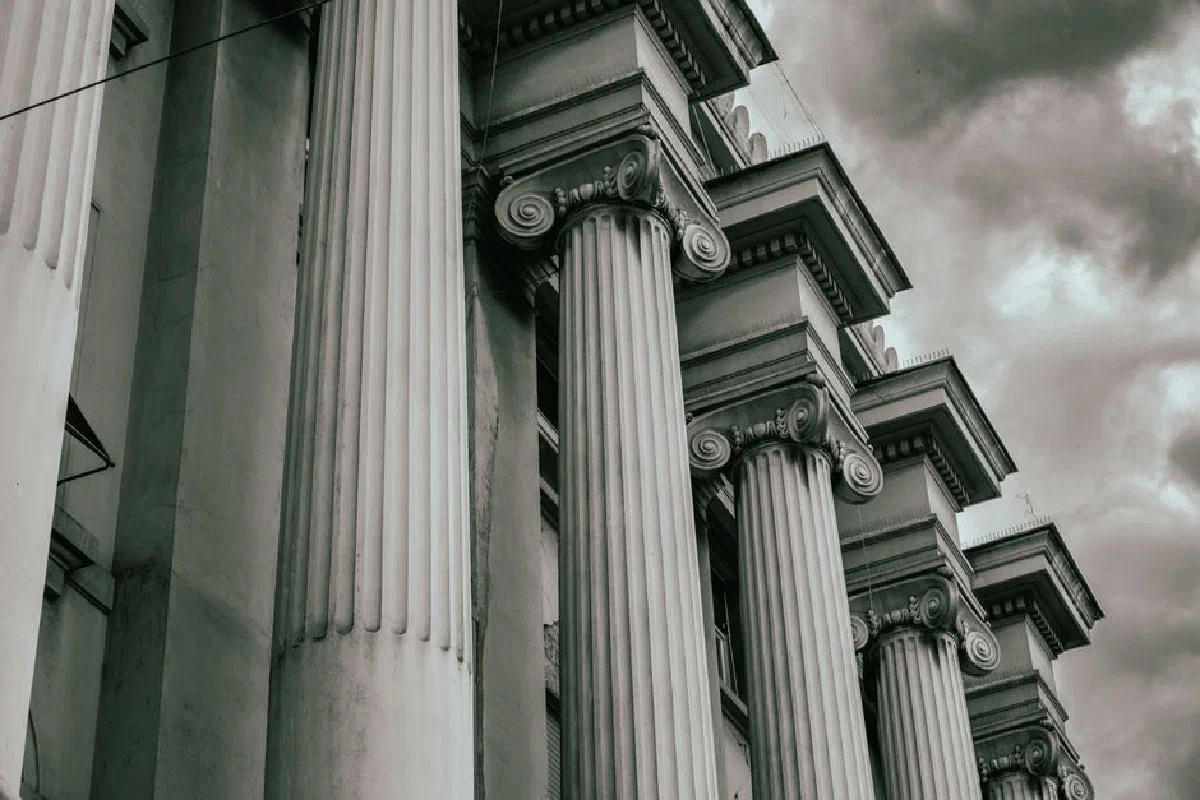 Dramatic grayscale image of Greco-Roman columns against a cloudy sky.