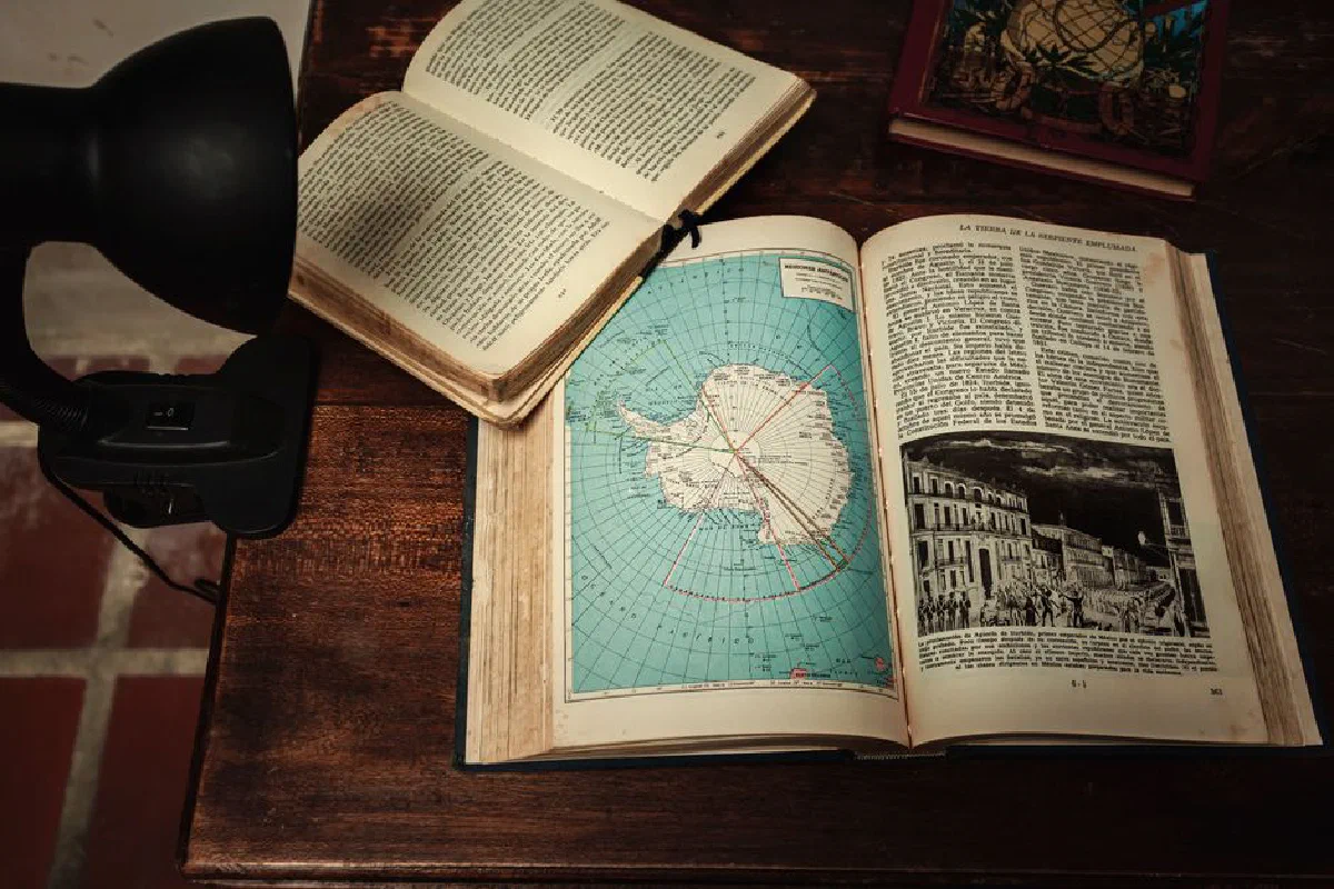 Open book with a map of Antarctica on a vintage wooden desk, under warm lighting.