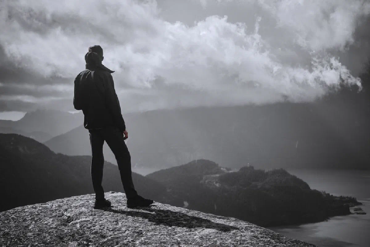 A man stands on a cliff in Squamish, BC, overlooking mountains and a lake in grayscale.
