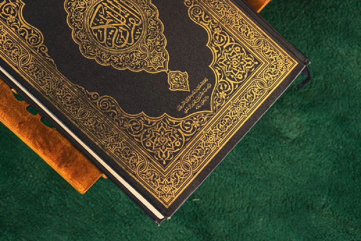 A Quran with an ornate golden design resting on a wooden stand against a green background.