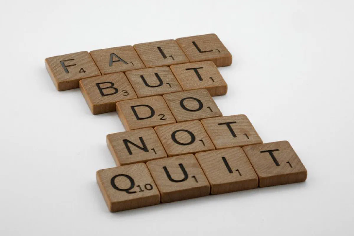 Close-up of Scrabble tiles forming the motivational phrase 'Fail but do not quit' on a white surface.