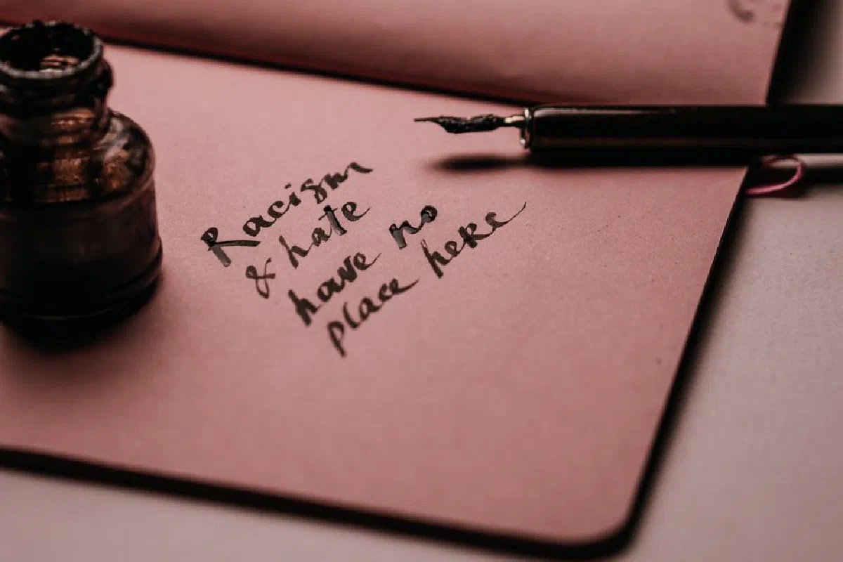 Ink pen and bottle on pink paper with motivational quote against racism and hate.