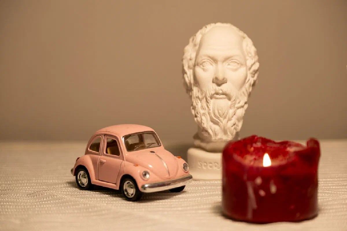 Artistic setup of a pink toy car, bust statue, and candlelight creating a nostalgic vintage ambiance.