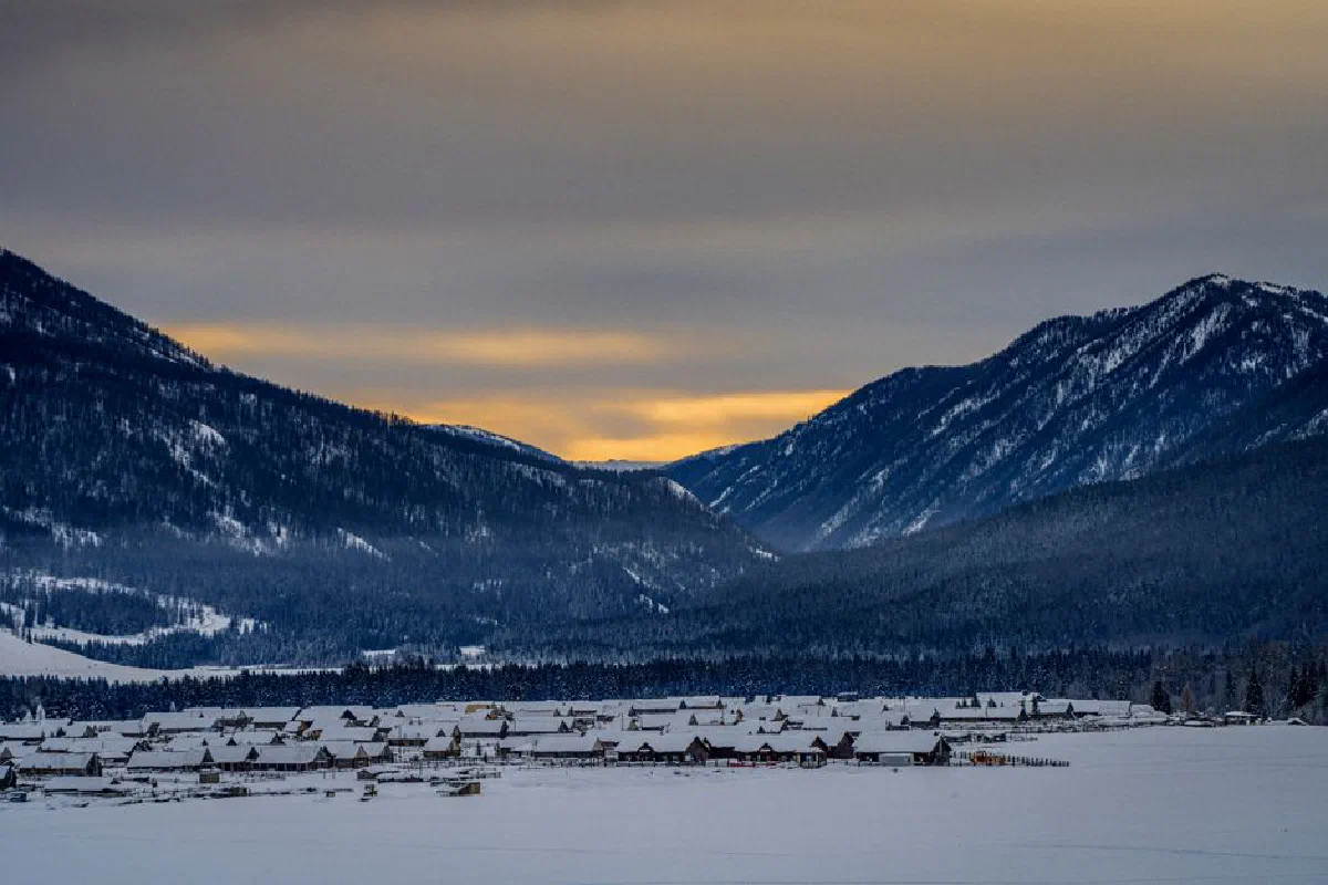 A serene snow-covered village nestled between majestic mountains during a beautiful sunset in winter.