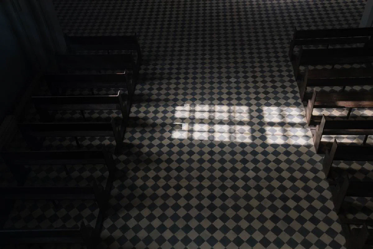Sunlight casts geometric patterns on a church's tiled floor viewed from above.