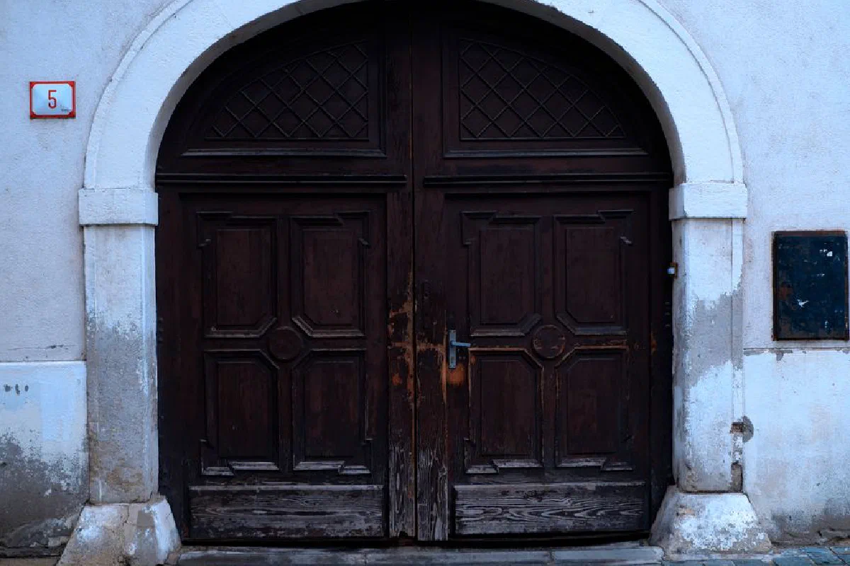 Aged wooden double doors with a white arched frame showcasing vintage charm.