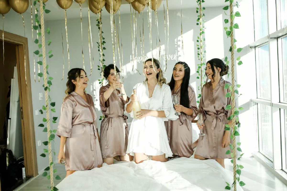 Bride and bridesmaids celebrating with champagne indoors. Joyful wedding preparation moment.