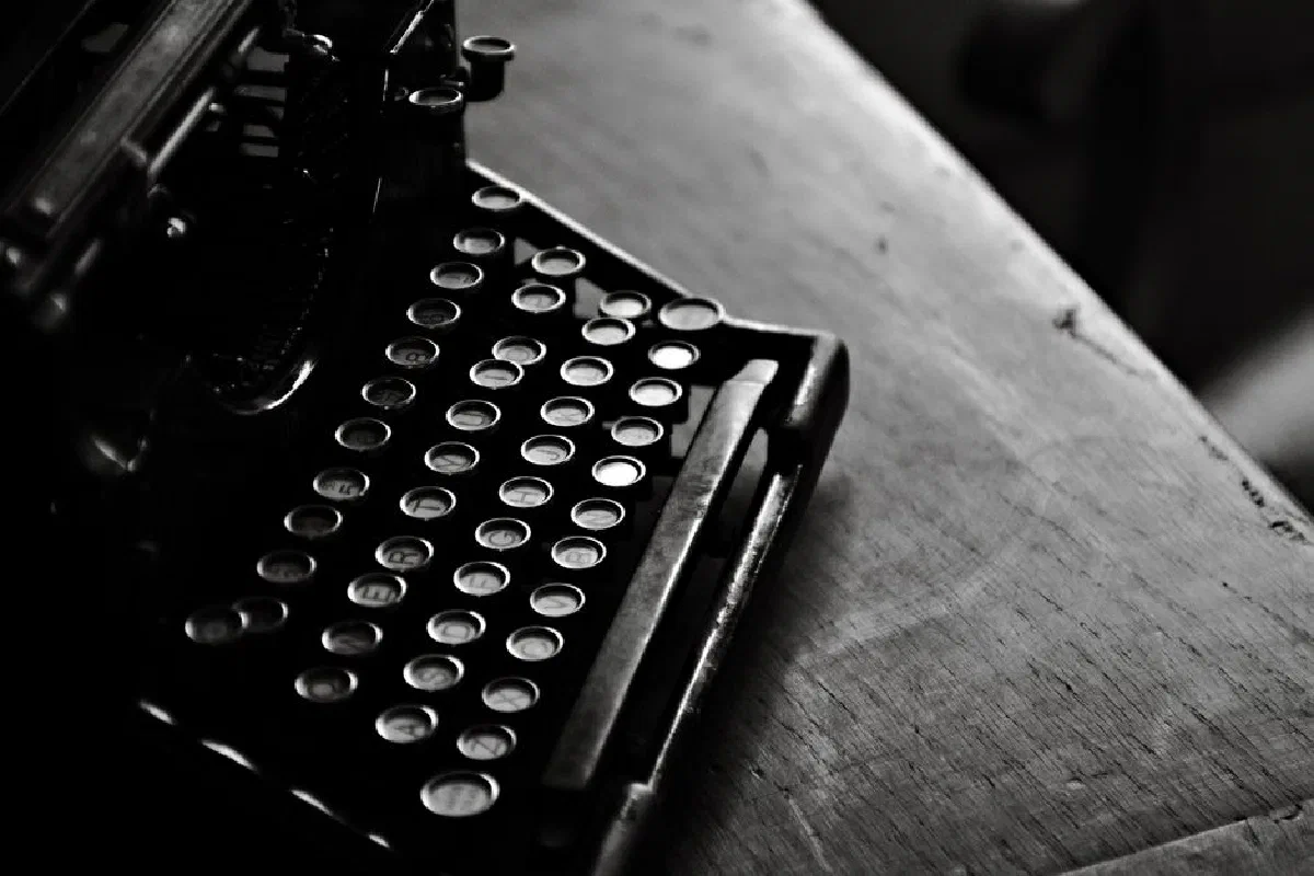 A classic black vintage typewriter in moody black and white on a wooden desk.