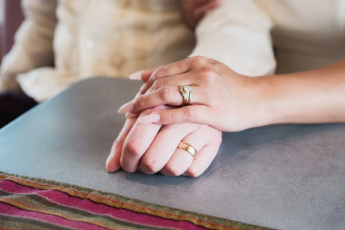 Close-up of two people holding hands warmly on a table, showcasing rings.