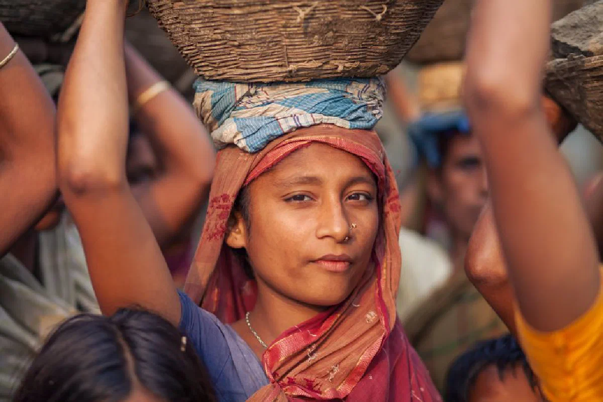 A woman in traditional attire carries a basket on her head in rural Bangladesh.