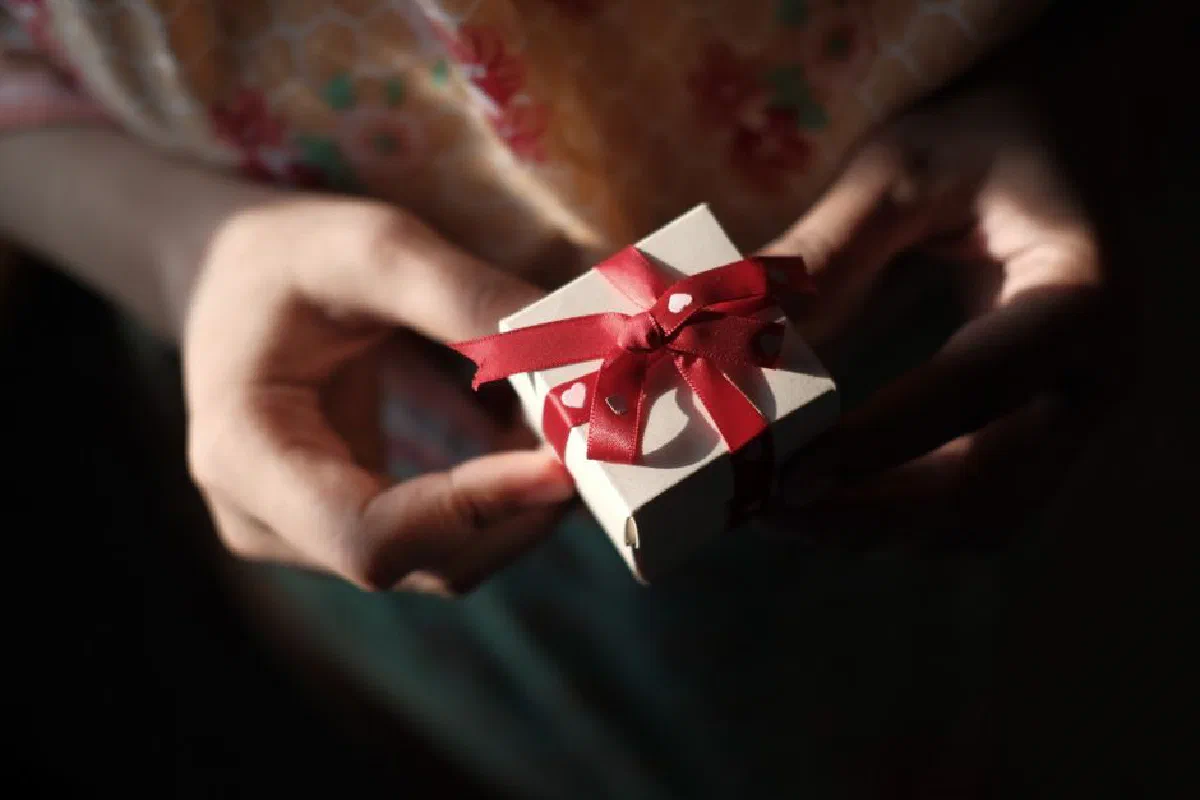 Close-up of hands holding a gift box wrapped with a vivid red ribbon, capturing a moment of giving.