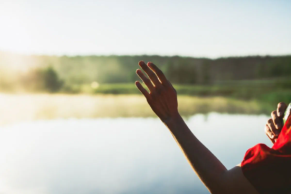 A serene moment showing an outstretched arm reaching towards nature by a calm lake.