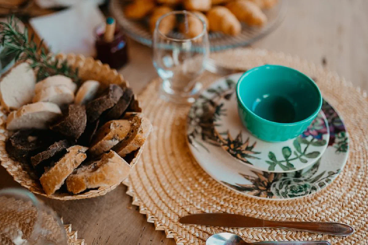 Cozy breakfast setup with various breads and ceramic tableware on a woven placemat.