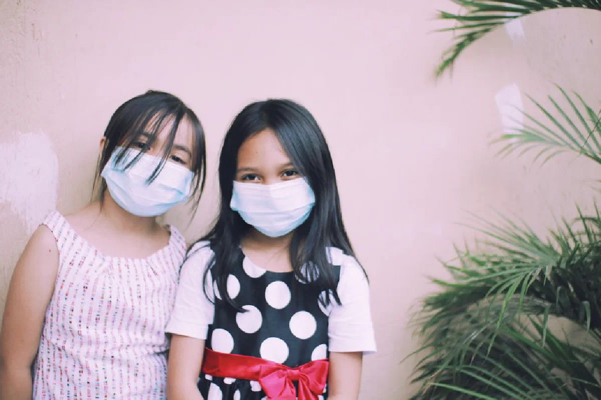 Two young girls wearing protective masks smiling outdoors. Health safety concept.