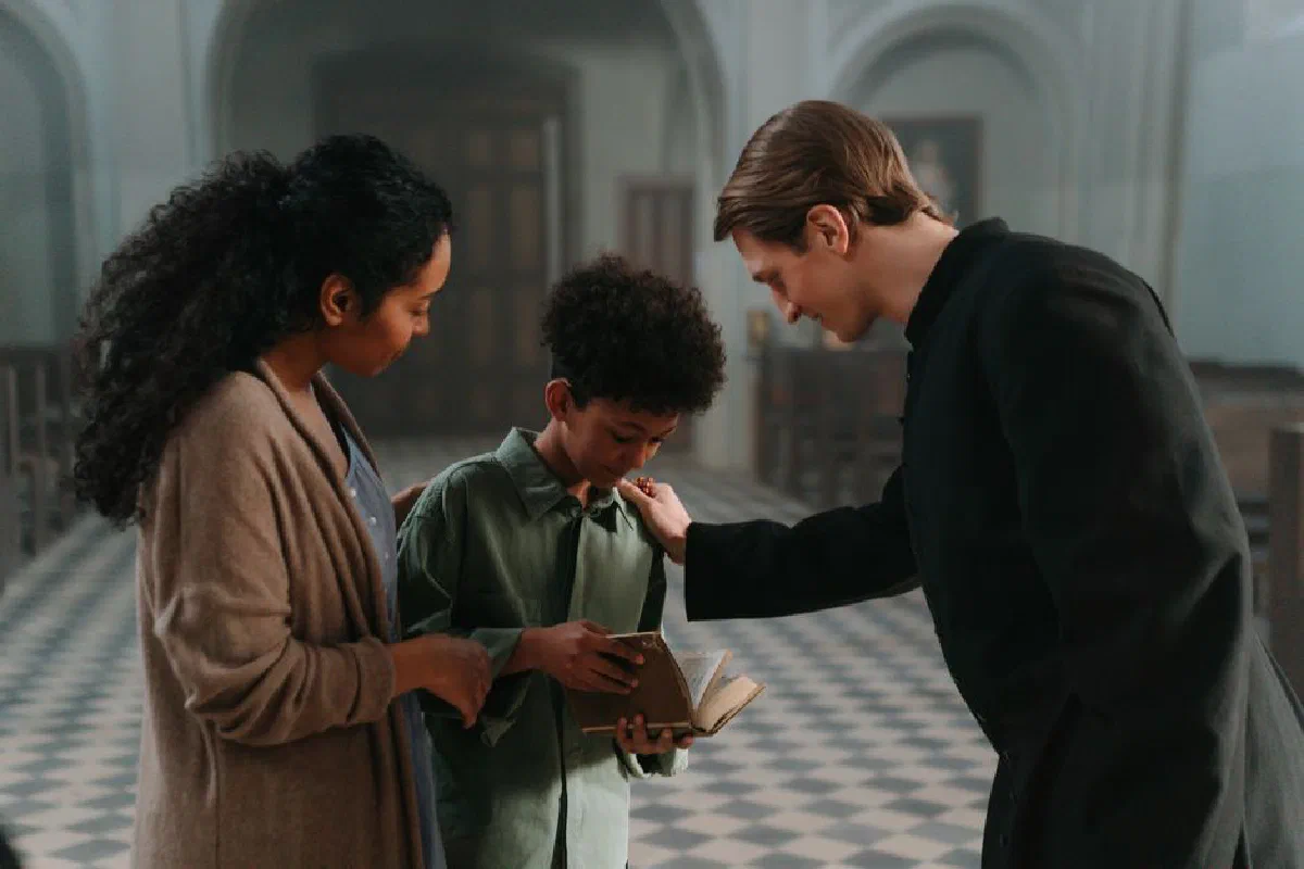 A priest blesses a mother and son inside a serene church setting.