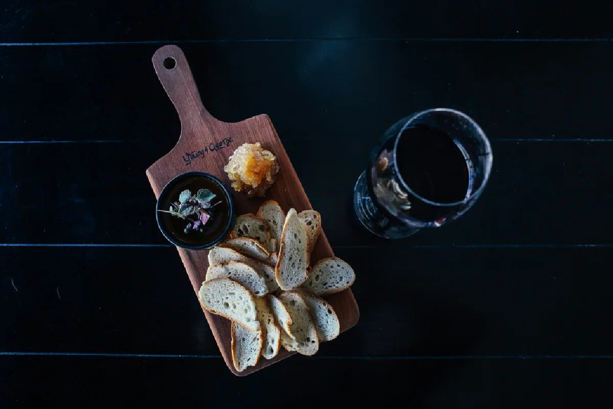 Top view of a cutting board with bread slices, herbs, and wine, creating a rustic snack setup.