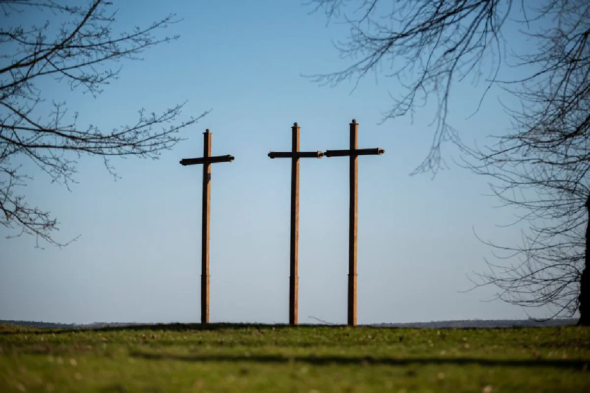 Peaceful landscape featuring three wooden crosses against a clear sky.