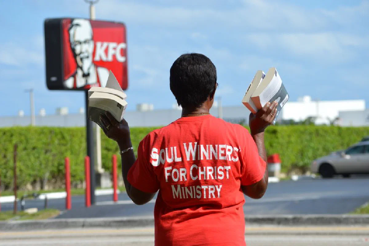 Back view of a person in red t-shirt holding books near a KFC sign.