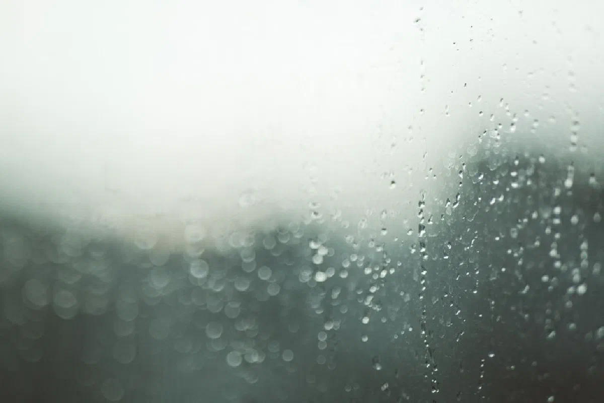 Close-up view of a window with raindrops and a soft bokeh background, creating an abstract texture.