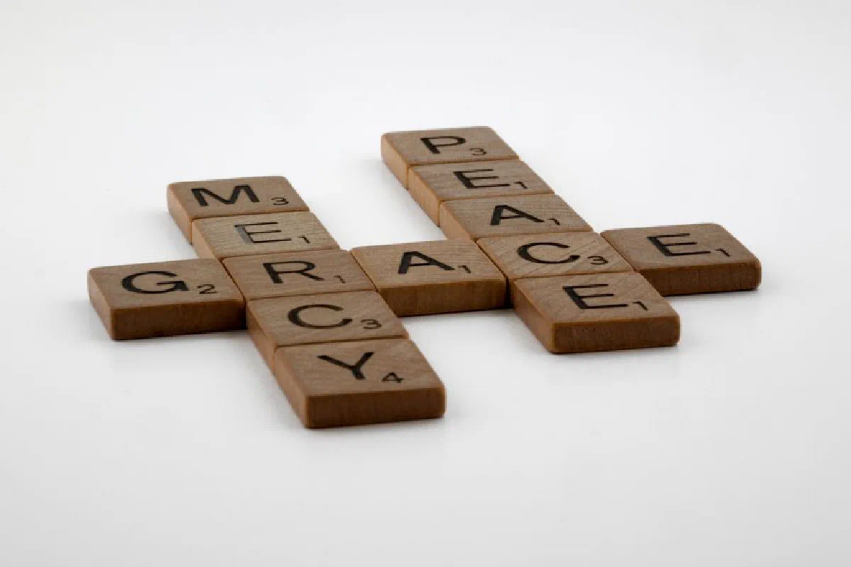 Wooden Scrabble tiles spelling 'grace', 'mercy', and 'peace' on a white surface.