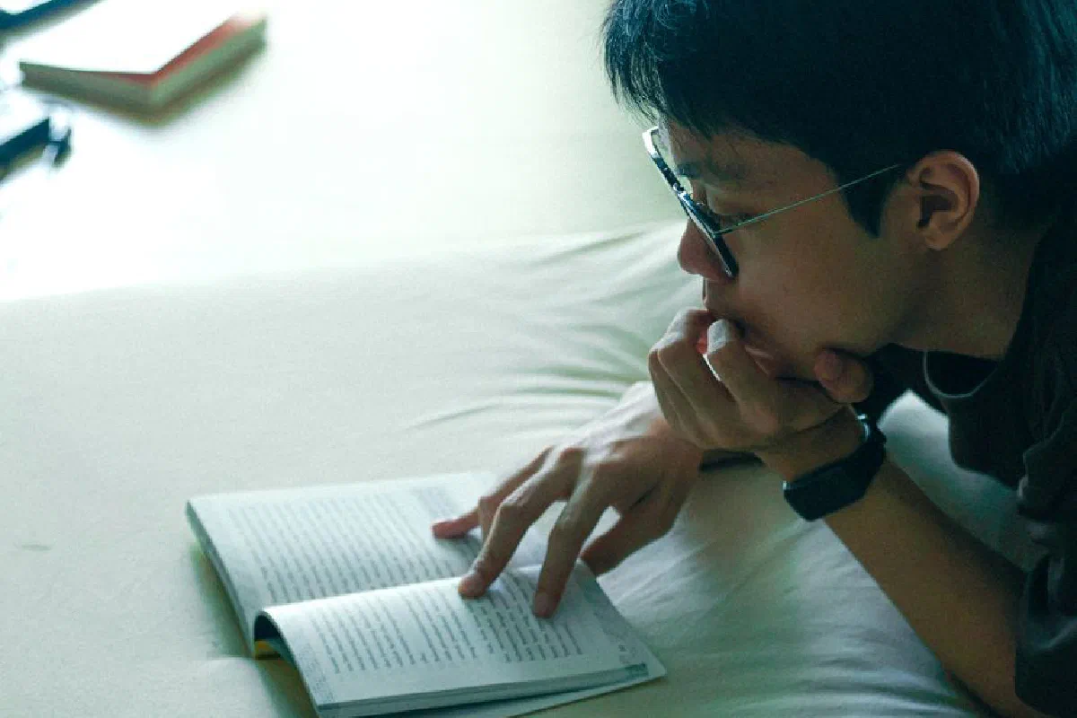 Young adult reading a book indoors in Jakarta, focusing on learning and relaxation.