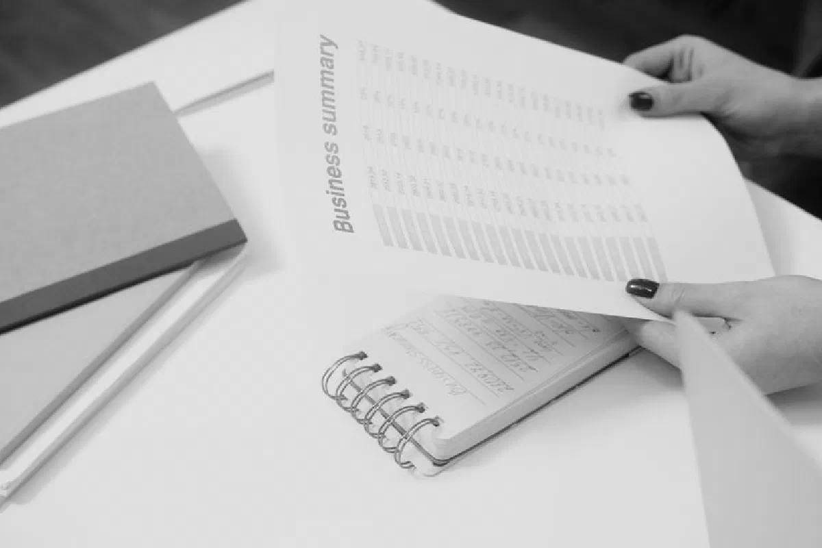 Black and white image of a businesswoman reviewing a business summary on paper.