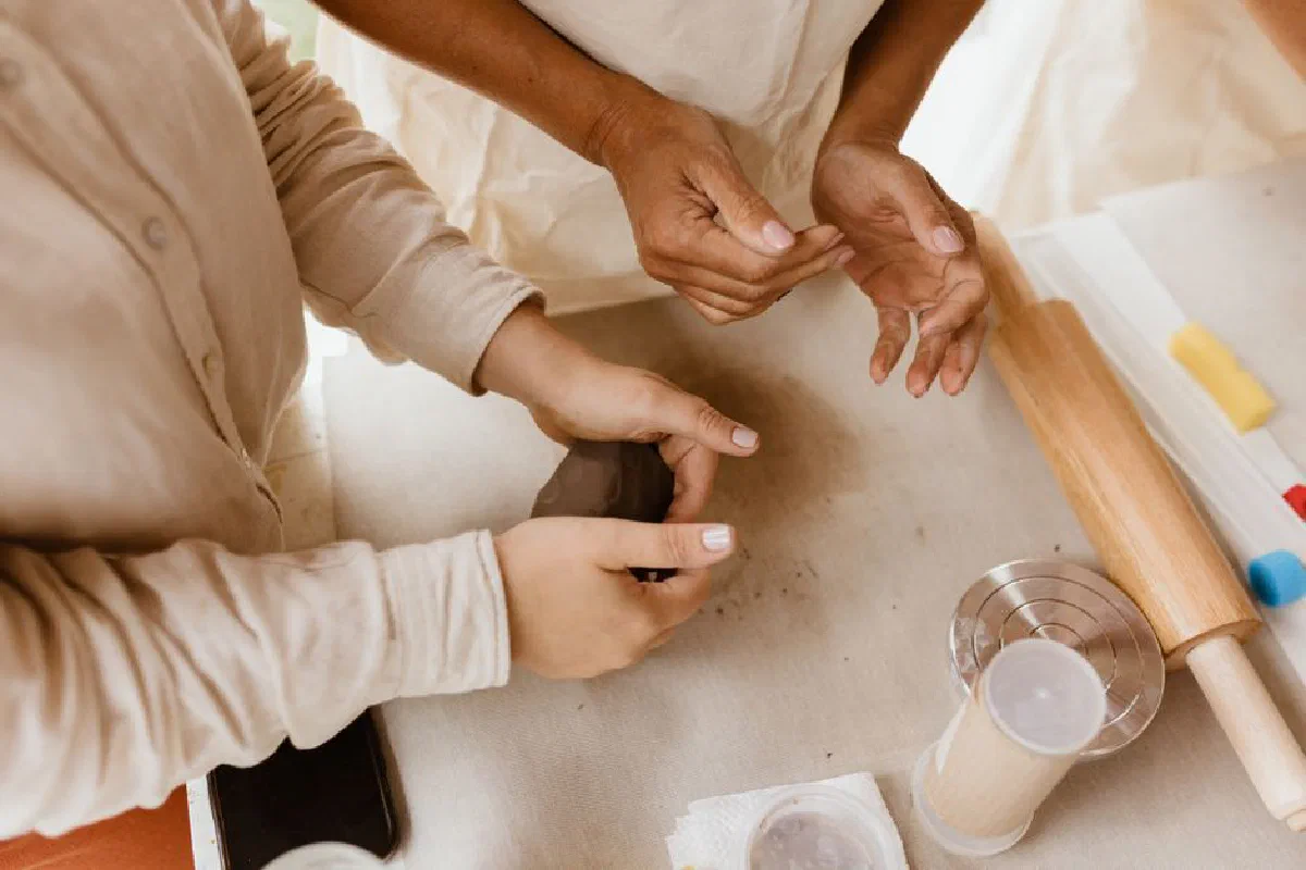 Close-up of hands engaged in molding clay, showcasing artisan skills with rolling pin and crafting tools.