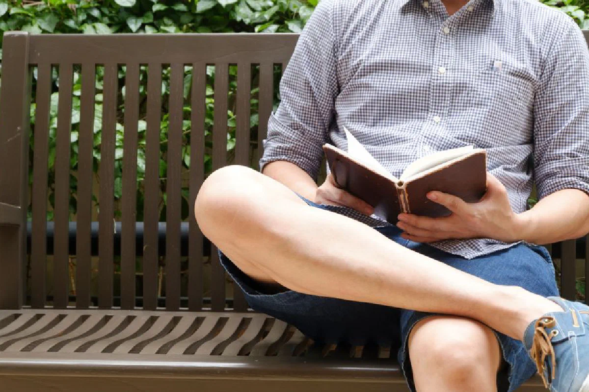A man relaxing and reading a book on a bench outdoors, enjoying a leisurely afternoon.