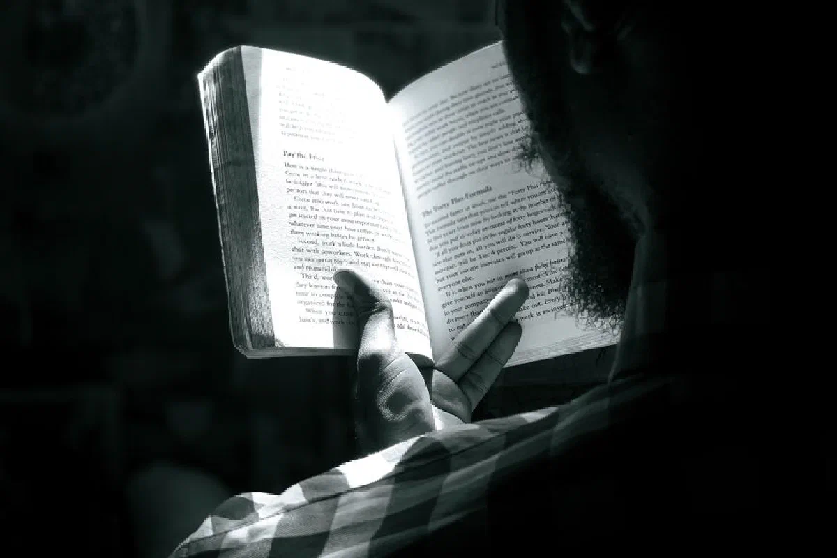 Black and white photo of a bearded man reading a book from behind, creating a moody atmosphere.