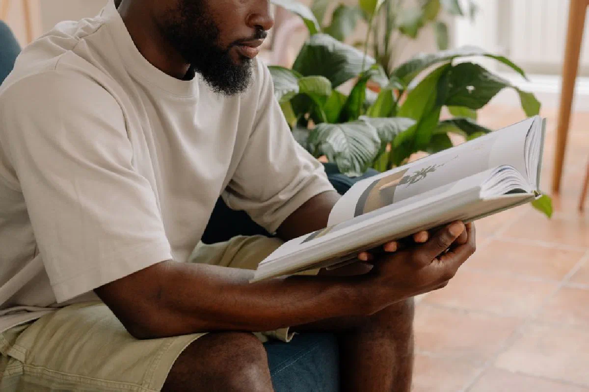 A man reading a book on a couch surrounded by lush indoor plants, creating a serene atmosphere.