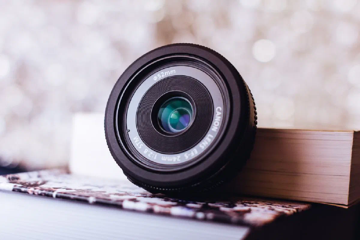 Detailed close-up of a Canon camera lens resting on books, surrounded by a soft bokeh backdrop.
