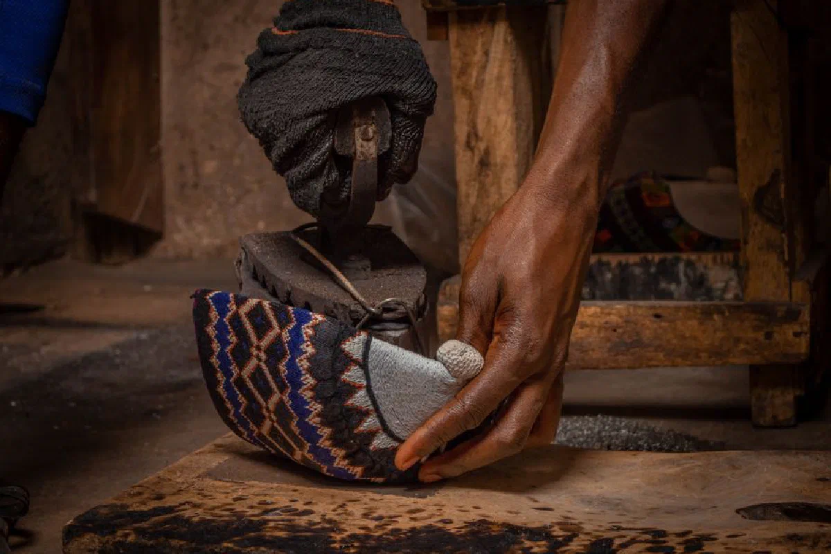 Close-up of artisan hands crafting a traditional shoe in a rustic workshop setting.
