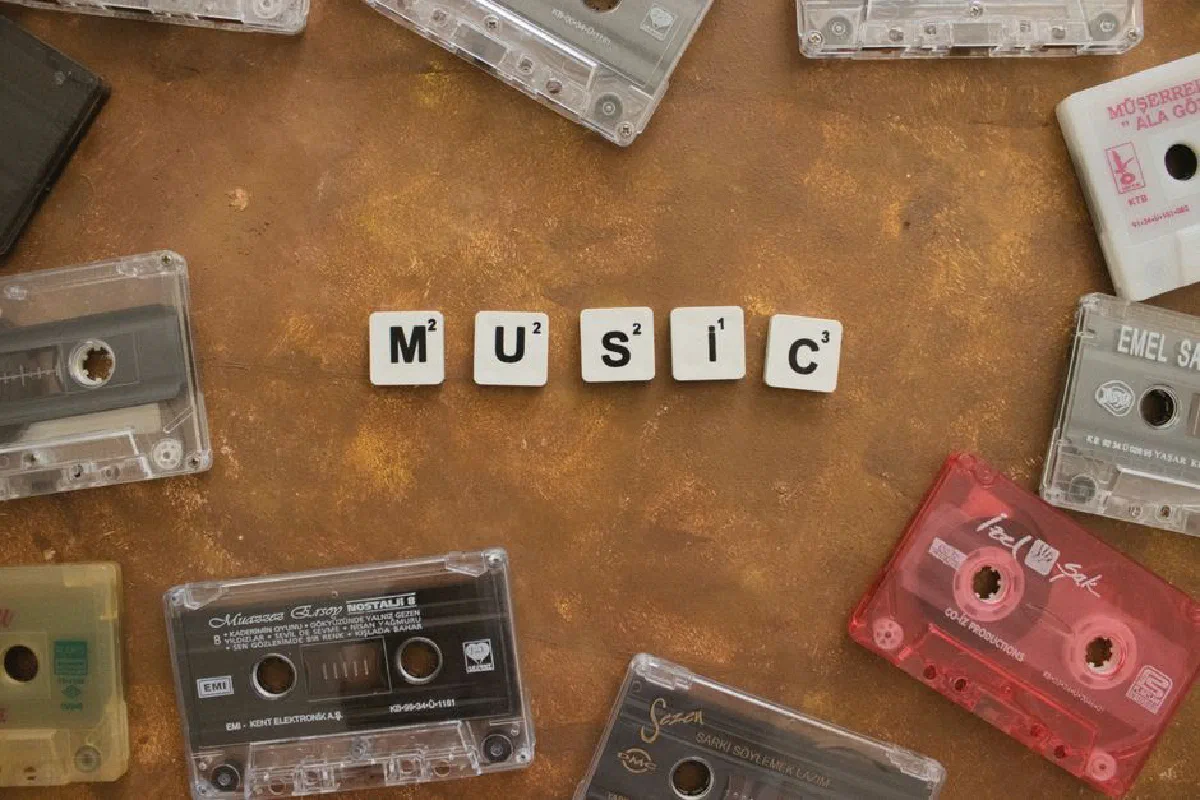 Retro cassette tapes arranged with Scrabble tiles spelling 'Music' on a brown background.