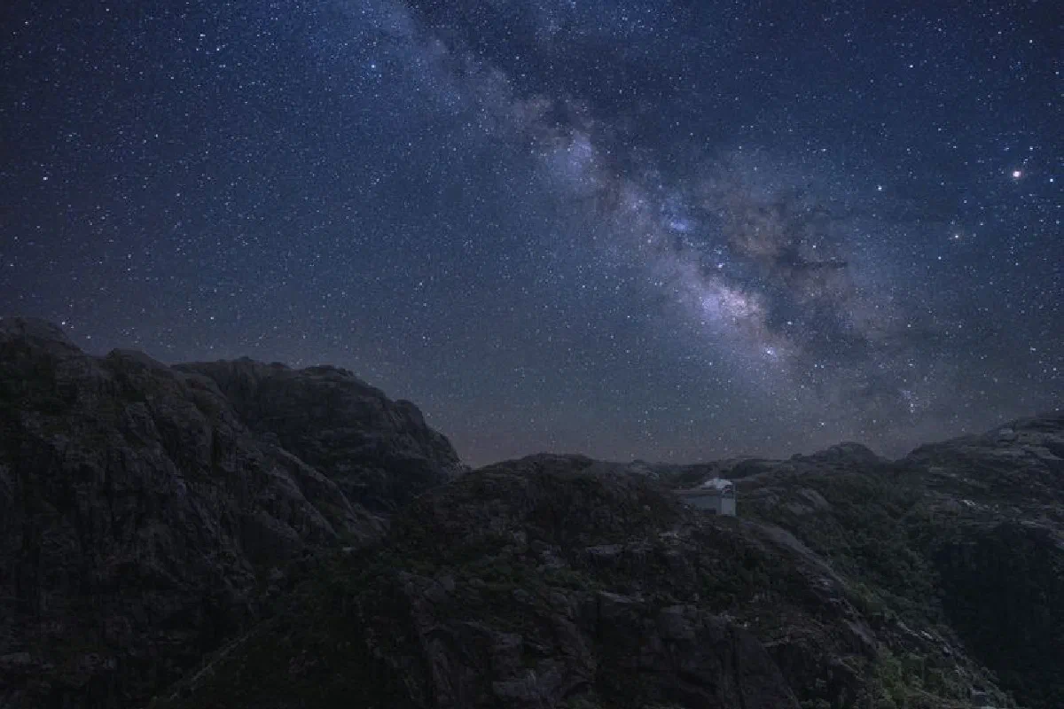 Bright glowing stars shining over dark night sky in high rocky mountainous terrain